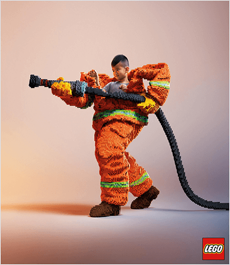Il s'agit d'une photo d'une publicité LEGO qui montre un jeune garçon asiatique dans un uniforme de pompier en LEGO. L'uniforme est orange avec une bande vert fluo autour des poignets du manteau et du pantalon. Le pompier est debout avec un pied en arrière et tient un tuyau d'incendie, également en legos. La tête du garçon apparaît hors du haut de l’uniforme, qui est beaucoup plus large que lui et s’arrête autour des épaules. La photo a été prise sur un fond neutre uni. Le logo LEGO apparaît dans une case rouge en bas à droite. Talia Wolf dit que LEGO est un excellent exemple de marque qui utilise l'émotion dans la publicité.